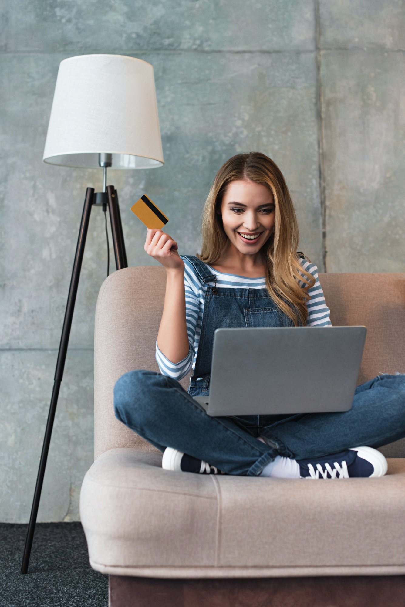 happy-beautiful-woman-holding-credit-card-in-hand-and-sitting-on-sofa-with-laptop.jpg